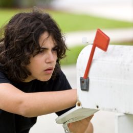 A young person looking into a white mailbox potentially stealing letters or packages