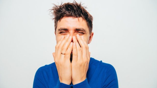 man covering his mouth while laughing at stupid jokes