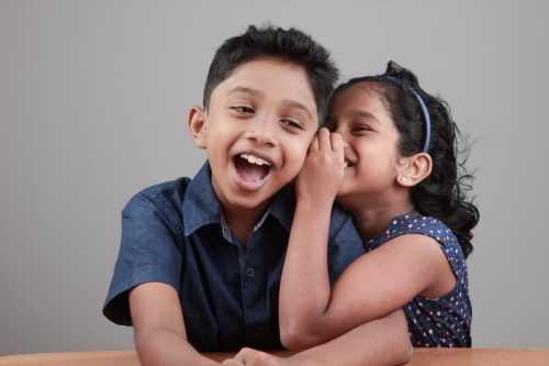 Little girl whispering a joke into the ear of a laughing little boy