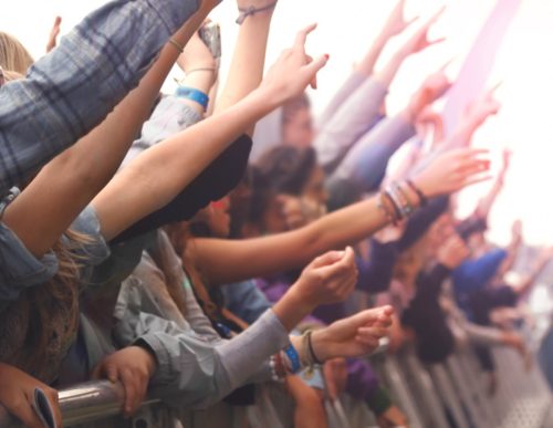 Abstract background of a cheering crowd of fans at concert with festivalgoers throwing hands in the air. Intentional blur added.