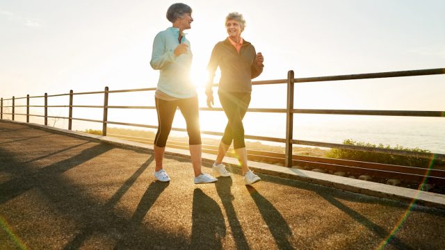 Shot of two senior women walking together in morning with sun shining from behind