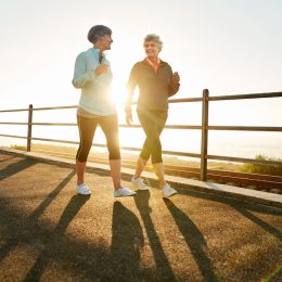 Shot of two senior women walking together in morning with sun shining from behind