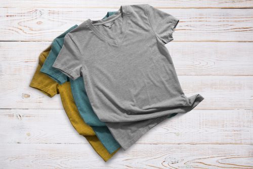 Mustard, tela, and gray ladies' v-neck t-shirts on a light wood background.