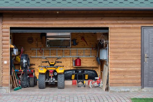 Facade front view open door ATV quad bike motorcycle parking messy garage building with wooden siding at home driveway backyard and lawn path. House warehouse for tools and equipment . Garage sale.