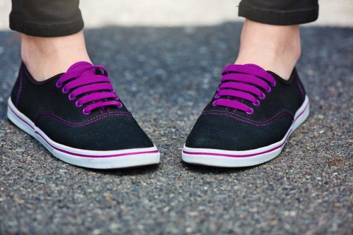 Woman's feet turned in, wearing black sneakers with purple shoelaces