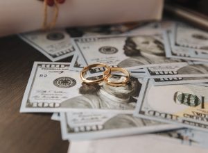 Two gold wedding bands sitting on top of a pile of hundred dollar bills.
