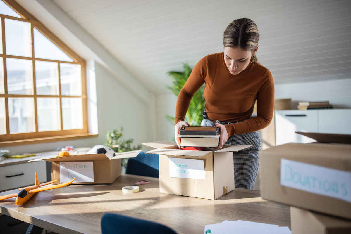 A young woman decluttering in her home and packing items into boxes for donation.