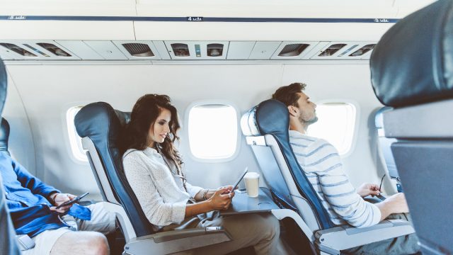 Young woman sitting in the aisle seat on an airplane using a digital tablet with two males on either side.