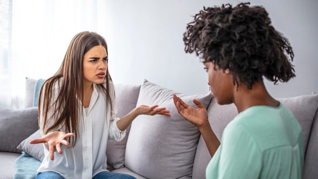 A young woman sitting on her couch looking offended by her female friend.