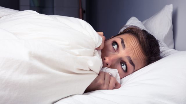 A woman scared in bed pulling the sheets up to her face