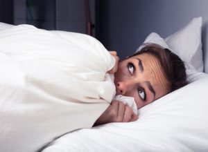 A woman scared in bed pulling the sheets up to her face