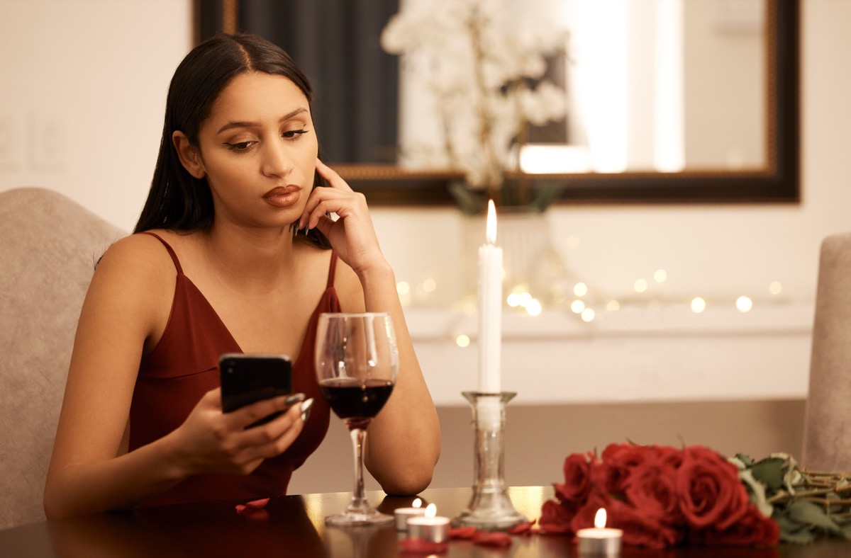 Wine, restaurant and sad woman with smartphone on date app waiting for communication. Serious, unhappy or angry girl fine dining alone with her cellphone reading bad or fail message on valentines day