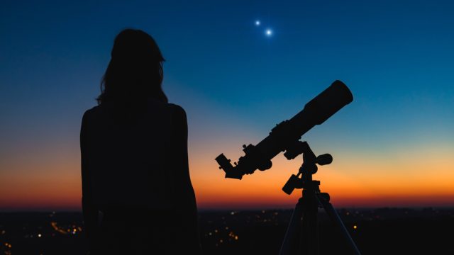 A woman standing next to a telescope and looking up into the night sky