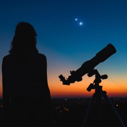 A woman standing next to a telescope and looking up into the night sky