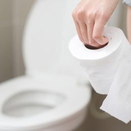 Close up of a woman walking towards the toilet holding toilet paper