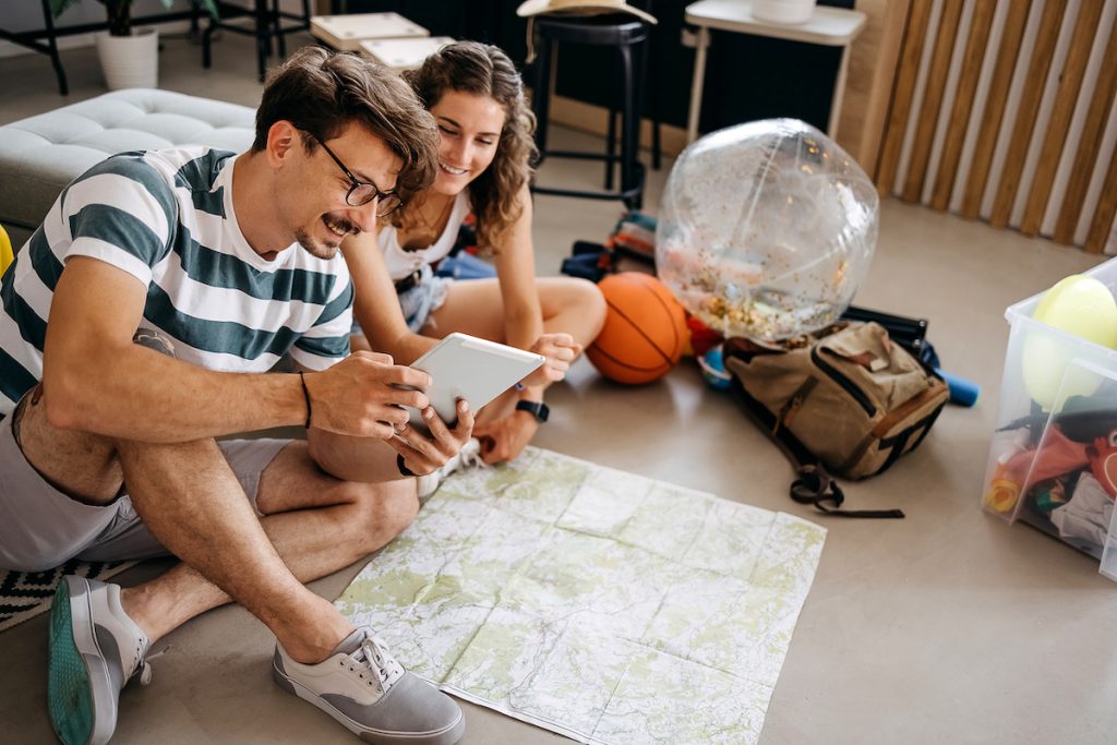 Couple planning a vacation trip sits on the floor looking at a map and a tablet