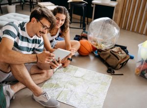 Couple planning a vacation trip sits on the floor looking at a map and a tablet