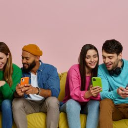 Studio shot of young people dressed in colorful clothes using smart phones and communicating while sitting on couch together
