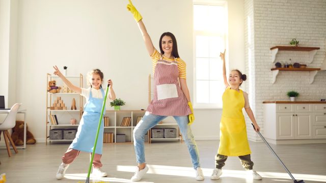 Happy family having fun while cleaning their house. Cute little children helping mom tidy up their apartment. Smiling young mother and daughters dancing together while mopping the floor at home