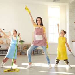 Happy family having fun while cleaning their house. Cute little children helping mom tidy up their apartment. Smiling young mother and daughters dancing together while mopping the floor at home