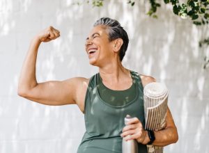 Happy older woman celebrating her fitness achievement after a great outdoor workout session, flaunting her strong bicep. Fit senior woman expressing her pride in her successful exercise routine.