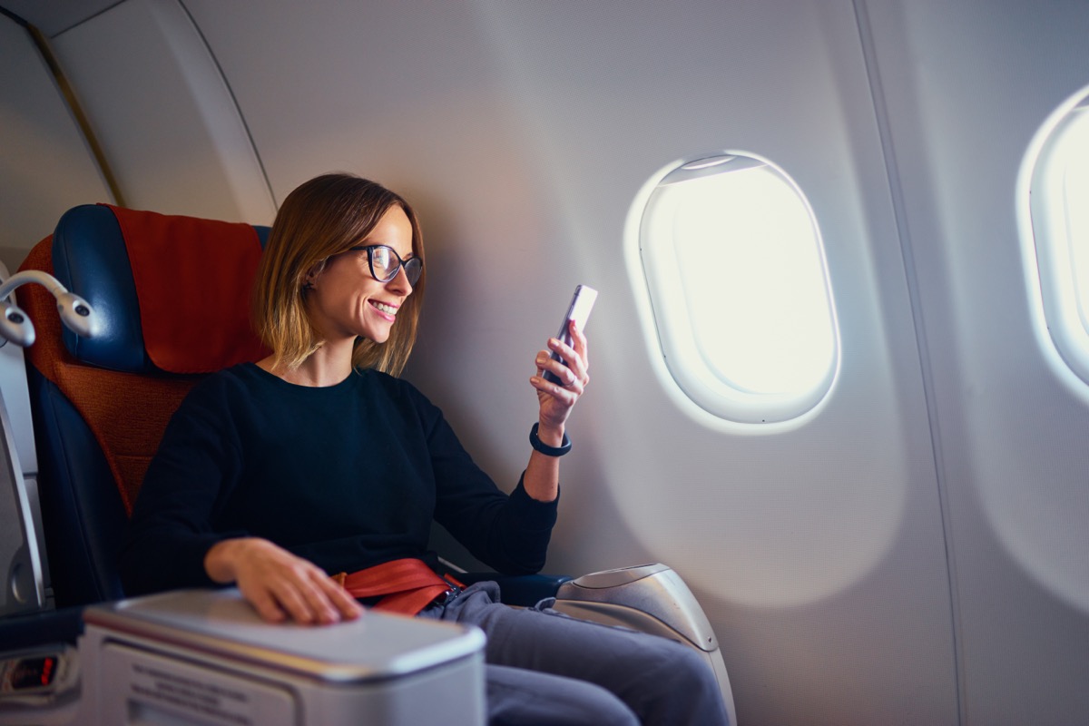 Happy woman using smartphone while sitting in airplane.