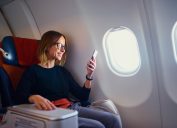 Traveling and technology. Flying at first class. Pretty young businees woman using smartphone while sitting in airplane.