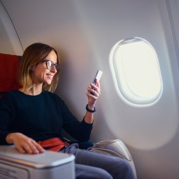 Traveling and technology. Flying at first class. Pretty young businees woman using smartphone while sitting in airplane.