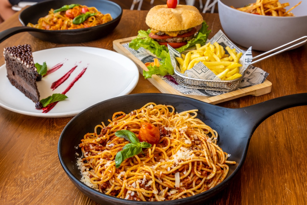 Food on wood table in restaurant, including pasta, burger and fries, and chocolate cake