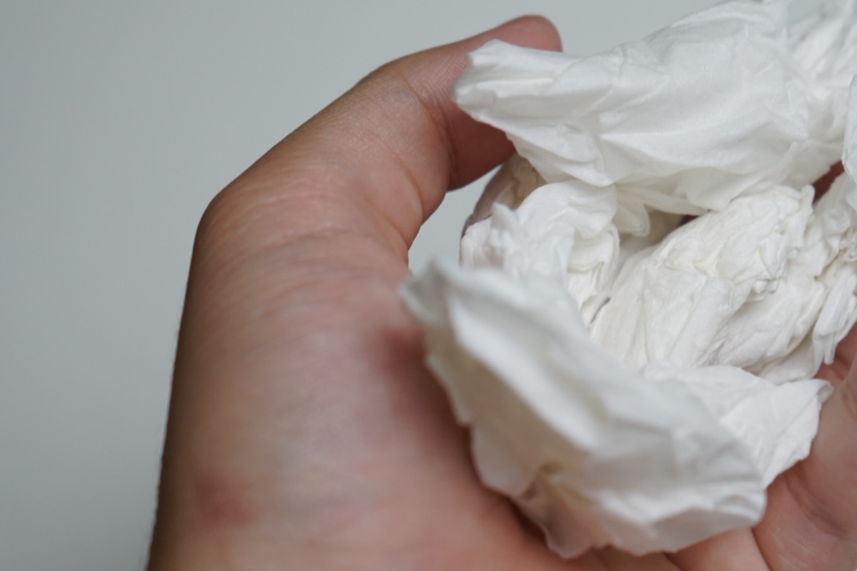 asian hand holding a wad of white tissue crumpled from use, on a white background