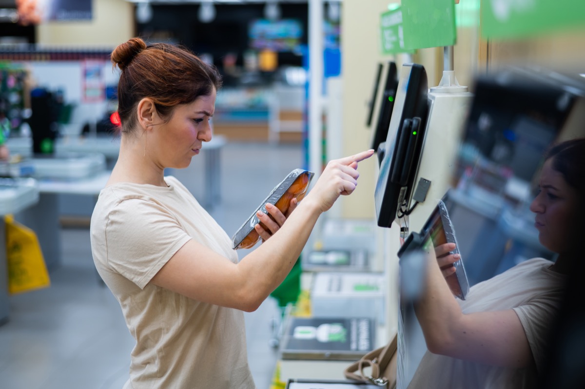A frustrated woman uses a self-checkout counter. The girl does not understand how to independently buy groceries in the supermarket without a seller