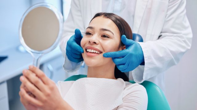 Dentist, mirror and woman check smile after teeth cleaning, braces and dental consultation. Healthcare, dentistry and happy female patient with orthodontist for oral hygiene, wellness and cleaning