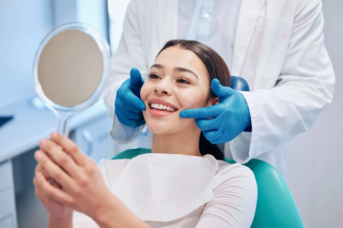 Patient at the dentist holding a mirror smiling while dentist points to her teeth