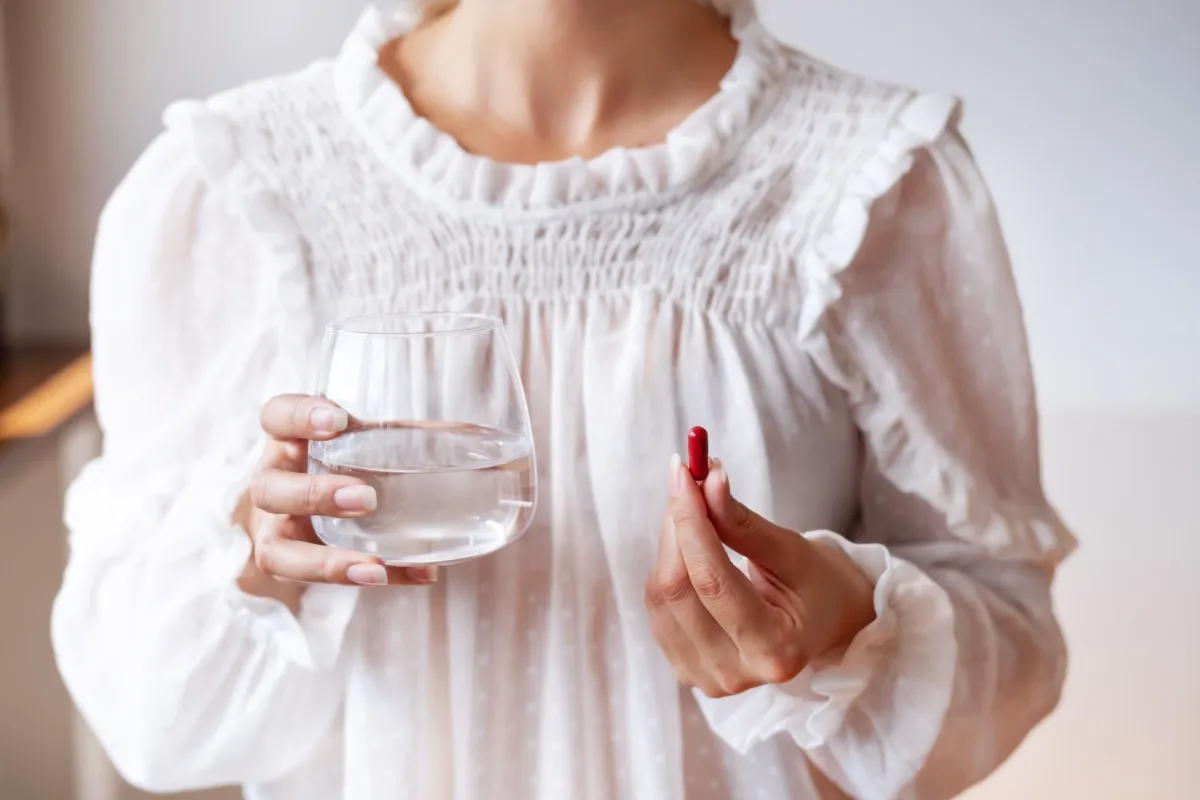 Woman in white blouse holding a red pill in one hand and a glass of water in the other