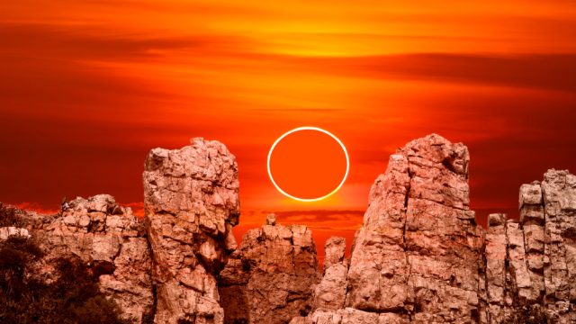 An annular solar eclipse rising over rock cliffs