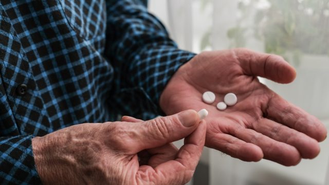 Close up of an elderly man's hands with pills. The concept of retirement life. The morning of an elderly person begins with taking pills and nutritional supplements.