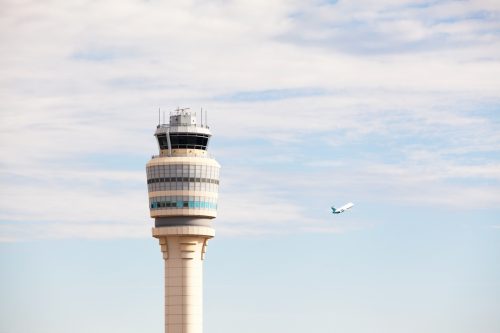 The air traffic control tower at Atlanta's Hartsfield-Jackson International Airport (ATL) with a plane taking off to the right. This airport is the world's busiest and this tower handles nearly one million planes each year. Two other airplanes are semi-visible in the sky, but very small.