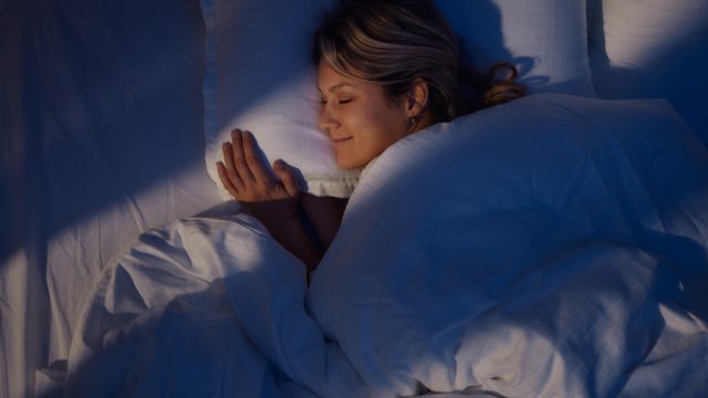 High angle view of young woman smiling while dreaming in bed at night.