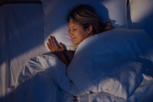 High angle view of young woman smiling while dreaming in bed at night.