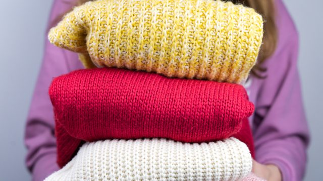 Woman holds warm knitted sweaters. Closet cleaning. Seasonal clothes. Donations. Close-up. Selective focus.