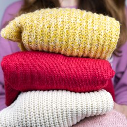 Woman holds warm knitted sweaters. Closet cleaning. Seasonal clothes. Donations. Close-up. Selective focus.