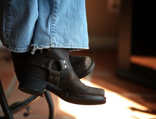 Close up of the bottom of a pair of woman's boot-cut jeans paired with black boots