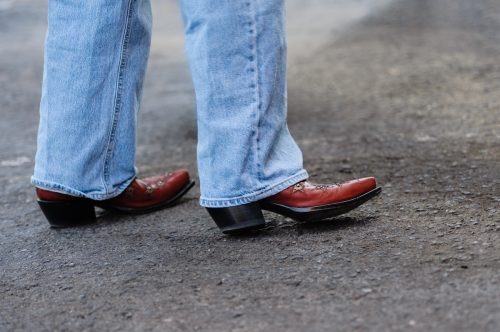 Close up of the bottom of a pair of light-colored boot-cut jeans and red cowboy boots