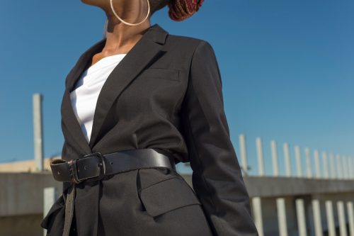 Close up of a woman outside wearing a long black blazer with a black belt and white shirt