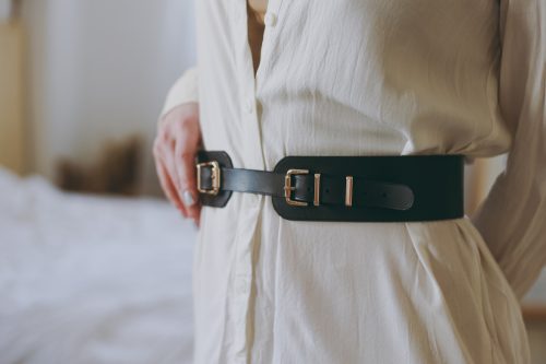 Close up of a woman wearing a long off-white shirt with a black corset-style leather belt