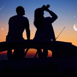 A couple sitting on the roof of a car with binoculars and watching the night sky and shooting stars