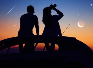 A couple sitting on the roof of a car with binoculars and watching the night sky and shooting stars