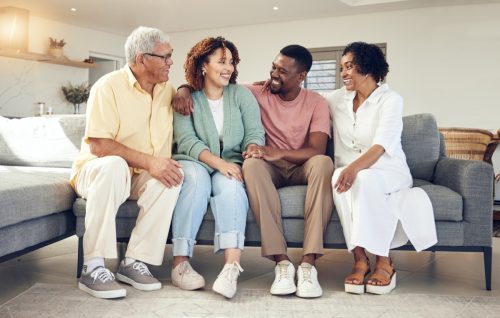 Happy family, parents and couple relax on a sofa, talking and laughing while bonding in a living room. Woman, man and seniors on a couch, happy and smile while enjoying weekend and retirement at home