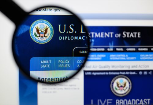 Photo of us department of state page on a monitor screen through a magnifying glass.