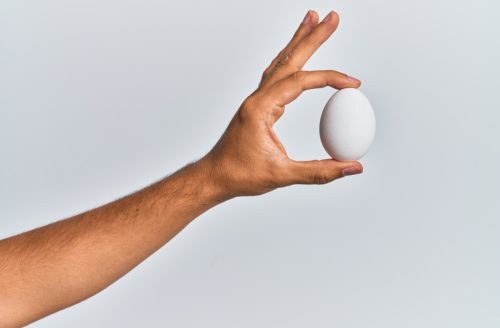 Hand holding raw egg over isolated white background.